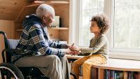 Older woman in a wheelchair holding hands with a young boy.